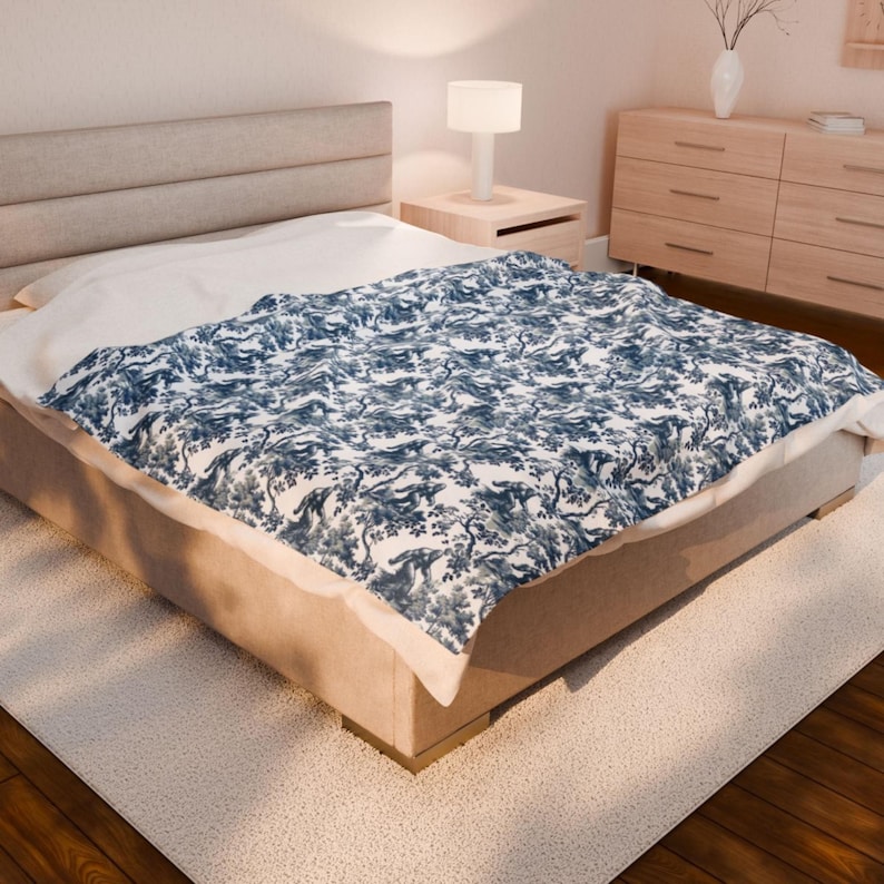 May include: A white bed with a blue and white patterned duvet cover. The bed is in a bedroom with a wooden dresser and a lamp on a bedside table.