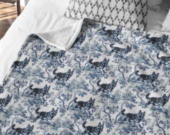 May include: A white and blue patterned fleece throw blanket with a repeating design of black dogs in a woodland setting.