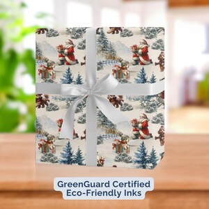 May include: Christmas-themed wrapping paper featuring Santa Claus, teddy bears, and dogs in a snowy landscape. The paper is wrapped around a gift and tied with a white ribbon. The text "GreenGuard Certified Eco-Friendly Inks" is visible.