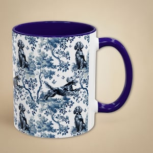Könnte beinhalten: Eine weiße Keramiktasse mit einem blauen und weißen Muster aus Hunden und Blumen. Die Tasse hat einen violetten Rand und einen violetten Henkel.
