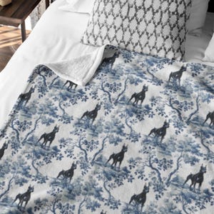 May include: A white throw blanket with a blue and white toile pattern featuring black dogs. The blanket has a soft, plush texture.