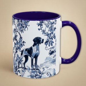 May include: A white ceramic mug with a blue and white floral pattern and a black and white German Shorthaired Pointer dog illustration. The mug has a purple rim and handle.