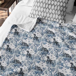Può includere: Una coperta a fantasia blu e bianca con un motivo ripetuto di cani e alberi. La coperta ha una consistenza morbida e soffice con una fodera in sherpa bianca. Il design ricorda i classici motivi toile.