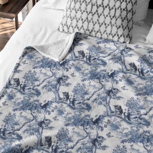May include: A white and blue fleece throw blanket with a repeating pattern of blue cats in trees and butterflies.