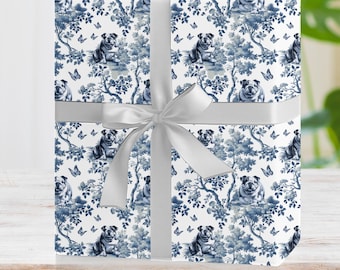 May include: A white gift wrap with a blue and white pattern of dogs, butterflies, and flowers. The gift wrap is tied with a silver ribbon.