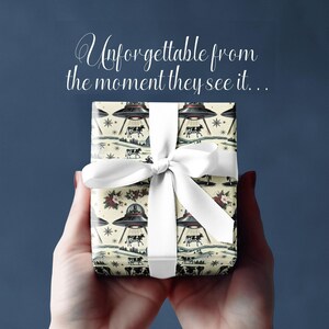 Pu&ograve; includere: Una scatola regalo bianca avvolta in carta con un motivo di dischi volanti e mucche. La scatola &egrave; legata con un nastro bianco e il testo "Unforgettable from the moment they see it..." &egrave; scritto sopra la scatola.