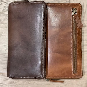 May include: Two leather wallets with zippers. The wallet on the left is brown and the wallet on the right is tan.