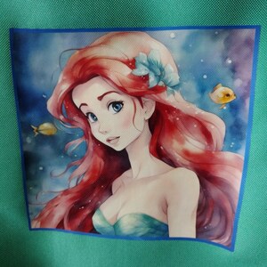 Peut inclure: Fond vert turquoise avec une image carr&eacute;e d'une sir&egrave;ne aux cheveux roux, aux yeux bleus et un haut turquoise. La sir&egrave;ne est entour&eacute;e d'eau bleue et de deux poissons jaunes. Une bordure bleue entoure l'image.