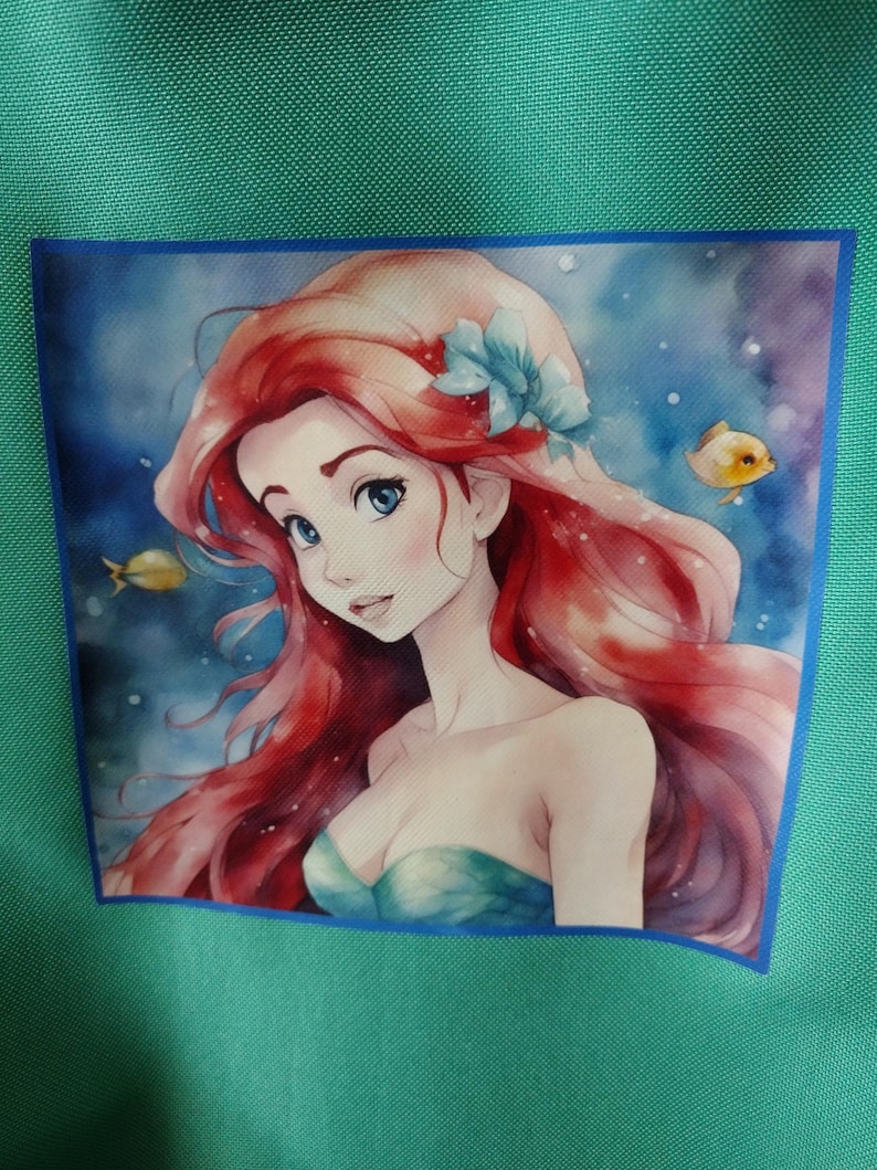 Peut inclure: Fond vert turquoise avec une image carr&eacute;e d'une sir&egrave;ne aux cheveux roux, aux yeux bleus et un haut turquoise. La sir&egrave;ne est entour&eacute;e d'eau bleue et de deux poissons jaunes. Une bordure bleue entoure l'image.