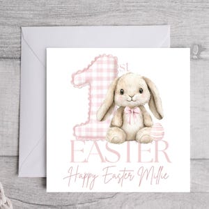 May include: A pink and white gingham 1 with a brown bunny holding a pink and white striped egg. The text "1st Easter" is below the number and bunny. The text "Happy Easter Millie" is below the text "1st Easter".