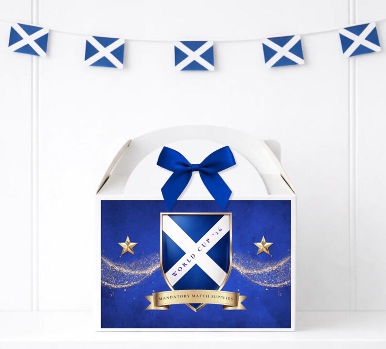 May include: A white box with a blue bow, adorned with a Scottish flag motif. The box displays a shield with the Scottish flag, gold stars, and the text "WORLD CUP '16" and "MANDATORY MATCH SUPPLIES". A garland of Scottish flags is suspended above.