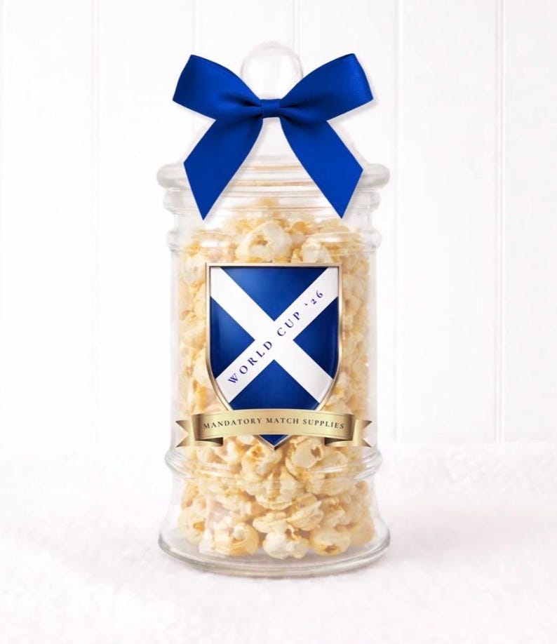May include: A glass jar filled with popcorn, adorned with a blue bow. The jar features a label with a Scottish flag design, the text "WORLD CUP '16", and "MANDATORY MATCH SUPPLIES".