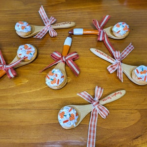 May include: Six wooden spoons with orange and white frosting and sprinkles, decorated with red and white gingham ribbon. The spoons are labeled "Pumpkin Spice".