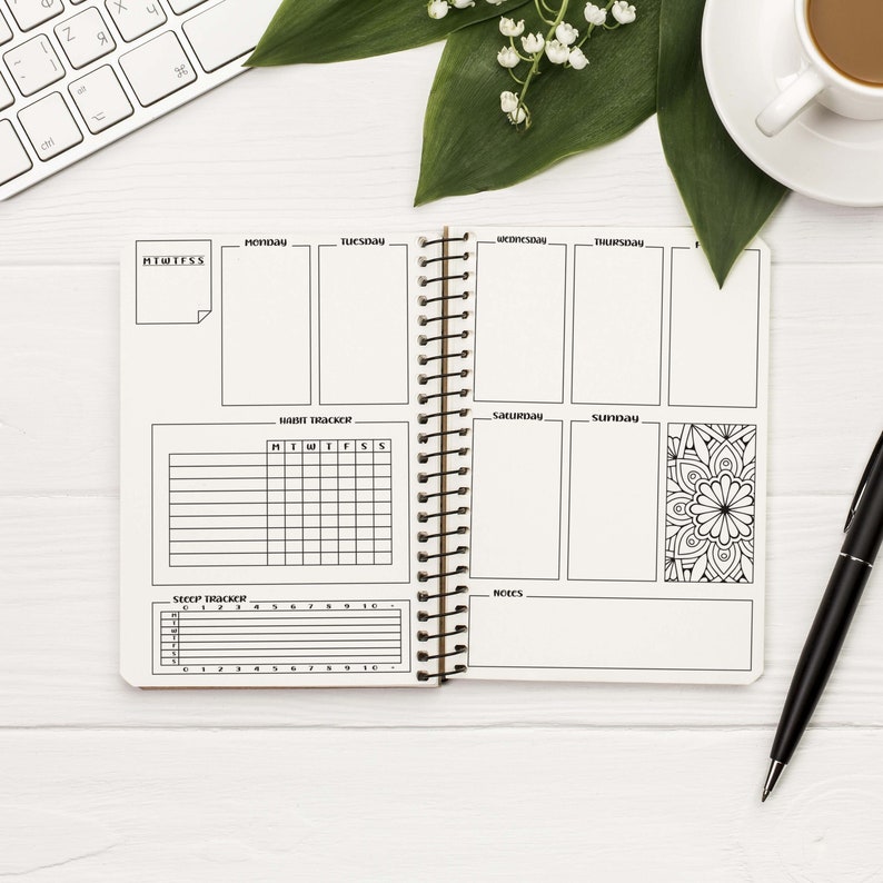 May include: An open planner with a weekly schedule, habit tracker, sleep tracker, and notes section. The planner has a black and white design with a floral mandala on the right page.