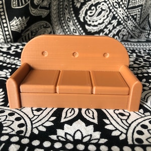 May include: A brown, three-seater sofa with a rounded back and three cushions. The sofa has three button tufts on the back.