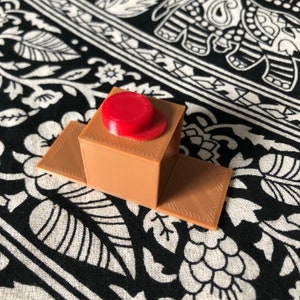 May include: A small, brown, 3D printed box with a red lid. The box is sitting on a black and white patterned fabric.