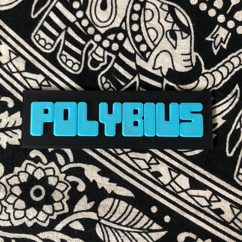 Pu&ograve; includere: Un cartello rettangolare nero con la parola "POLYBIUS" stampata in lettere blu.
