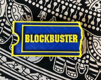以下が含まれることがあります： ブロックバスタービデオレンタルカードの青と黄色のプラスチック製レプリカ。カードは黄色の縁取りがあり、黄色の文字で「BLOCKBUSTER」と印刷されています。