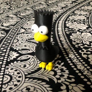 May include: A black 3D printed figurine of a cartoon bird with yellow eyes, beak, and feet. The bird has a spiky black hairdo.