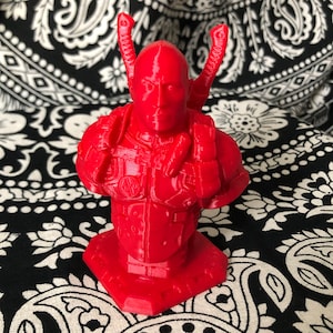 May include: Red 3D printed bust of a character wearing a detailed, futuristic suit with a helmet and two swords on the back.