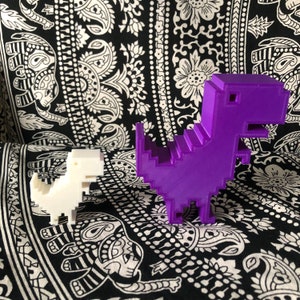 May include: Two 3D printed dinosaur figurines, one purple and one white, standing on a black and white patterned surface.