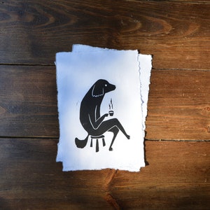 May include: Black and white illustration of a dog sitting on a stool and holding a cup of coffee.