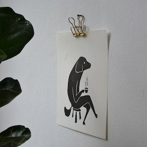 May include: Black and white illustration of a dog sitting on a stool and holding a cup of coffee. The dog is drawn in a simple, stylized manner.