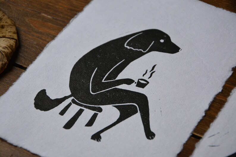 May include: Black and white illustration of a dog sitting on a stool and holding a cup of coffee. The dog is drawn in a simple, stylized manner.