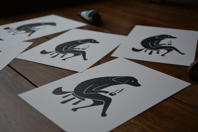 May include: Five black and white prints of a dog sitting on a stool and holding a cup of coffee. The dog is stylized and has a simple design.