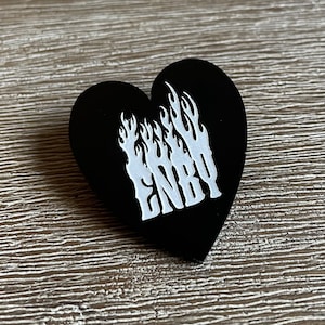 May include: Black heart-shaped pin with white flames and the word "ENBY" in a stylised font.