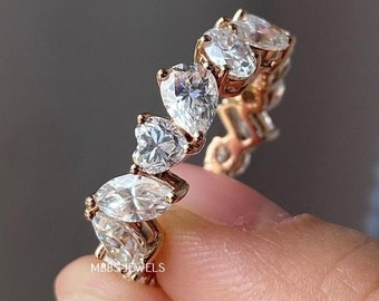 May include: A rose gold ring featuring a series of pear-shaped, clear gemstones. The ring is held by a hand, showcasing the intricate design and sparkle of the stones. The ring is from MBBS Jewellery Store.