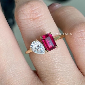 May include: A gold ring featuring a pear-shaped diamond and a rectangular ruby. The ring is worn on a finger.