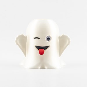 May include: A white ghost figurine with a winking eye and a red tongue sticking out. The ghost has two small arms and a rounded body.
