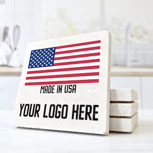 May include: A stack of square coasters with the American flag design. The coasters have the text "MADE IN USA" and "YOUR LOGO HERE" printed on them. The coasters are made of a light-colored, textured material.