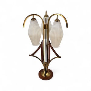 May include: A mid-century modern table lamp with three frosted glass shades. The lamp features a brass finish with wooden accents and a round wooden base. The shades have a ribbed texture, and the lamp has a unique, artistic design.