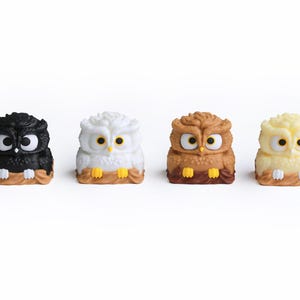 Puede incluir: Cuatro figuras de b&uacute;hos en negro, blanco, marr&oacute;n y amarillo. Cada b&uacute;ho tiene ojos grandes y est&aacute; posado en una rama marr&oacute;n. Los b&uacute;hos son peque&ntilde;os y decorativos, con un dise&ntilde;o de dibujos animados.