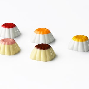 May include: Five small white ceramic pudding cups with different colored toppings. The toppings are red, orange, yellow, pink, and brown.