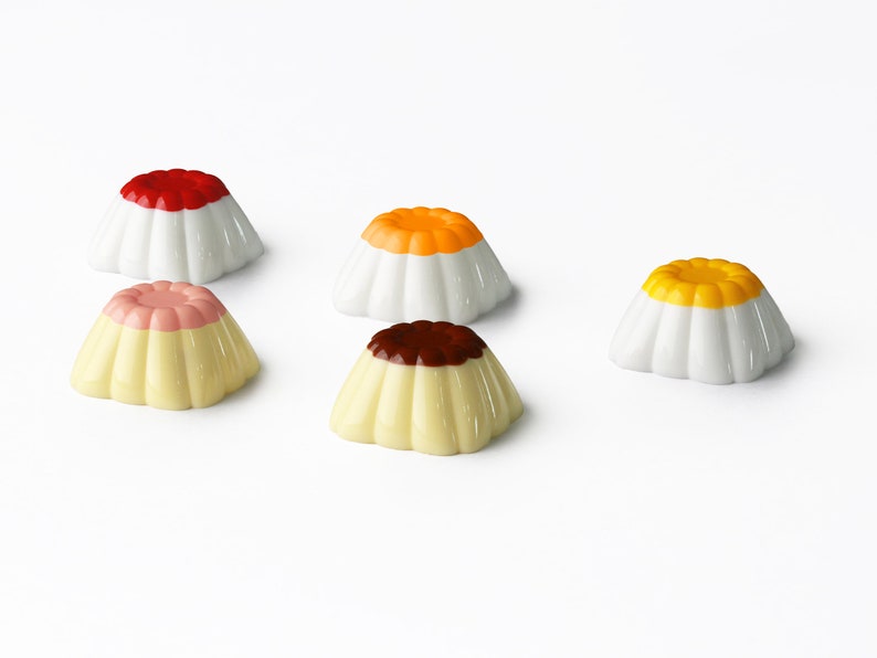 May include: Five small white ceramic pudding cups with different colored toppings. The toppings are red, orange, yellow, pink, and brown.