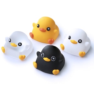 Pode incluir: Quatro pequenos brinquedos de pel&uacute;cia redondos em forma de pintinhos. Um &eacute; amarelo, um &eacute; branco, um &eacute; preto e um &eacute; transparente. Eles t&ecirc;m olhos pretos, bicos laranja e p&eacute;s laranja.