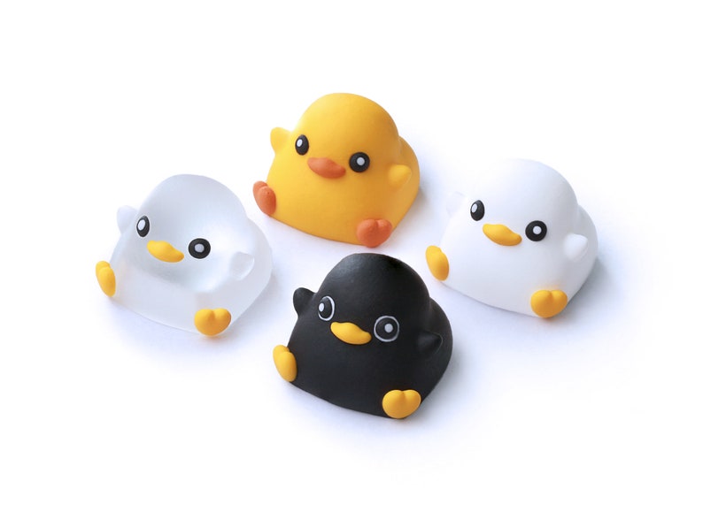 Pode incluir: Quatro pequenos brinquedos de pel&uacute;cia redondos em forma de pintinhos. Um &eacute; amarelo, um &eacute; branco, um &eacute; preto e um &eacute; transparente. Eles t&ecirc;m olhos pretos, bicos laranja e p&eacute;s laranja.