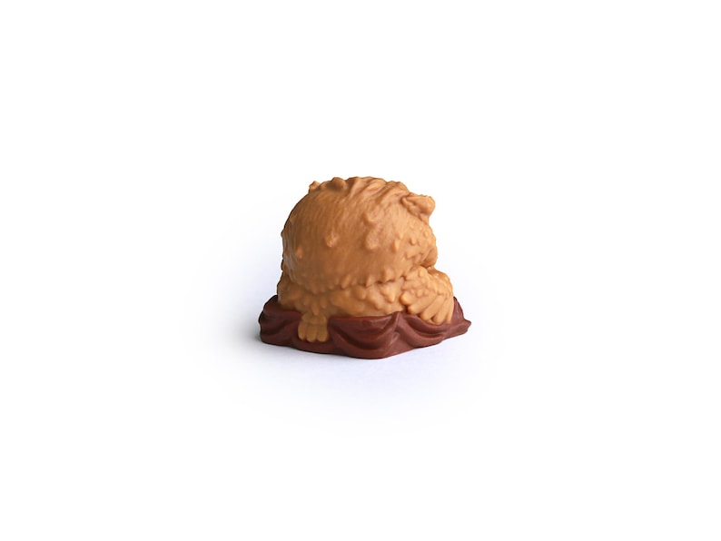 Puede incluir: Peque&ntilde;a escultura marr&oacute;n texturizada de un osezno, sentado sobre una base marr&oacute;n oscuro. El oso tiene una cabeza y un cuerpo redondeados con una textura detallada similar a la piel. La base tiene una apariencia arrugada.