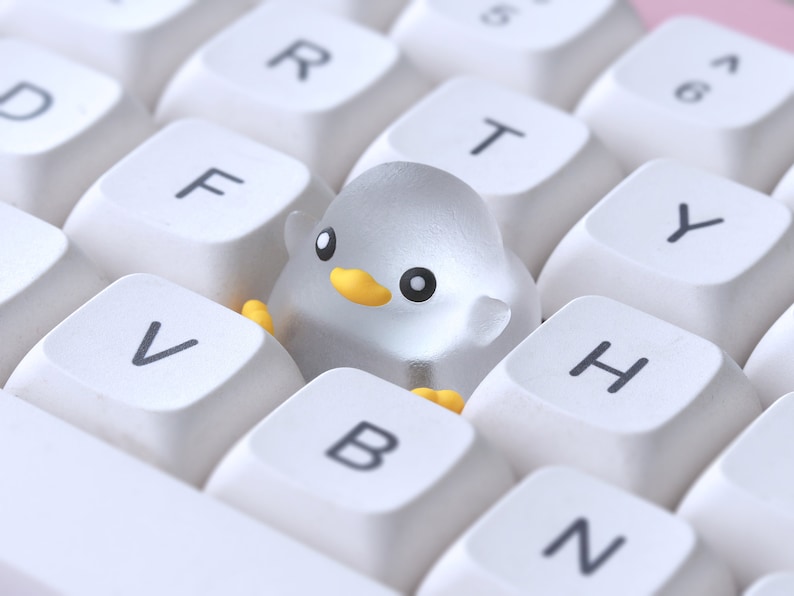 Pode incluir: Um teclado branco com uma figura de pinguim de pl&aacute;stico transparente sentada nas teclas F, V e B.