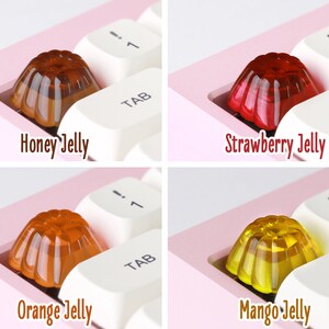 May include: Four different colored jelly keycaps for a keyboard. The keycaps are shaped like a dome and have a rippled texture. The colors are honey, strawberry, orange, and mango.