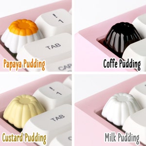 May include: Four different pudding-shaped keycaps for a keyboard. The keycaps are white, yellow, black, and orange. The keycaps are labeled "Papaya Pudding", "Coffe Pudding", "Custard Pudding", and "Milk Pudding".