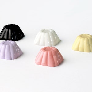 May include: Five small, round, colorful gelatin molds in various colors: black, white, light purple, light pink, and yellow.