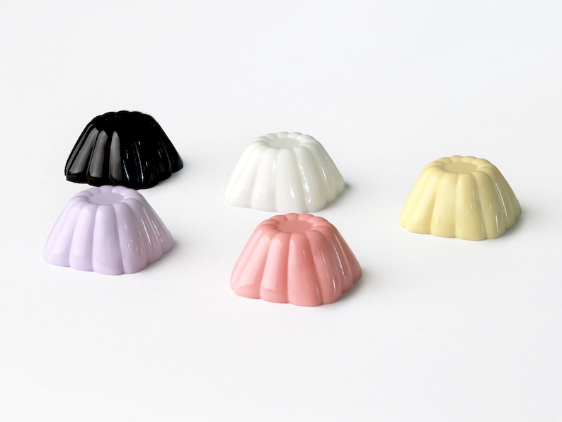 May include: Five small, round, colorful gelatin molds in various colors: black, white, light purple, light pink, and yellow.