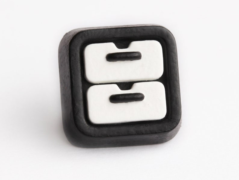 May include: A square, black button with a white design of two stacked drawers. Each drawer has a black handle. The button is likely for clothing or crafts.