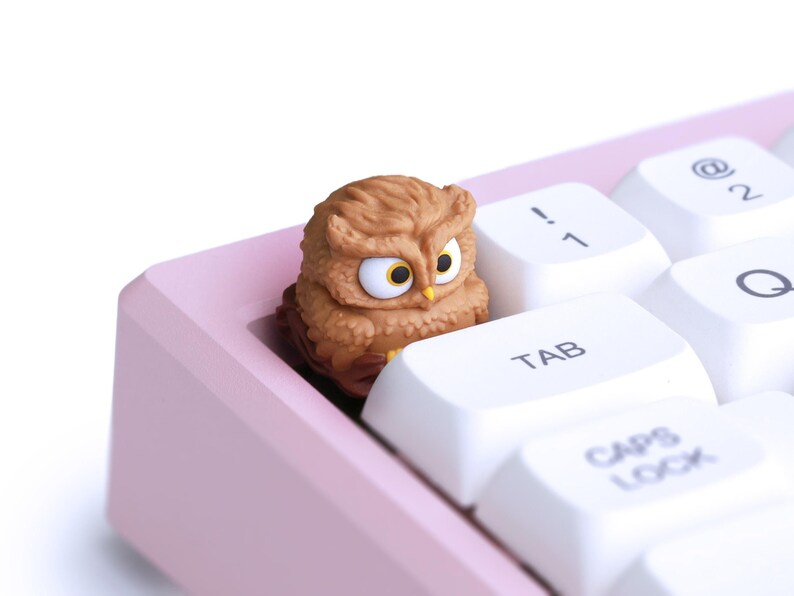 Puede incluir: Una tecla con forma de b&uacute;ho marr&oacute;n se encuentra en un teclado rosa. El b&uacute;ho tiene grandes ojos amarillos y texturas de plumas detalladas. Se ven teclas blancas con letras negras, incluida la tecla "TAB".
