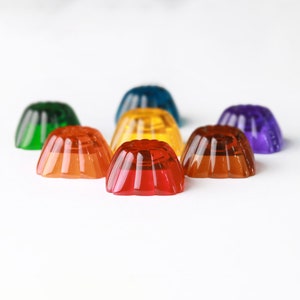 May include: A rainbow assortment of six colorful gelatin desserts in the shape of a dome. The colors are green, orange, yellow, red, purple, and blue.