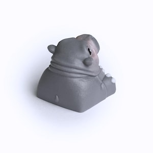 Puede incluir: Un keycap gris en forma de hipop&oacute;tamo con un acento blanco en la oreja. El keycap est&aacute; hecho de pl&aacute;stico liso y mate.